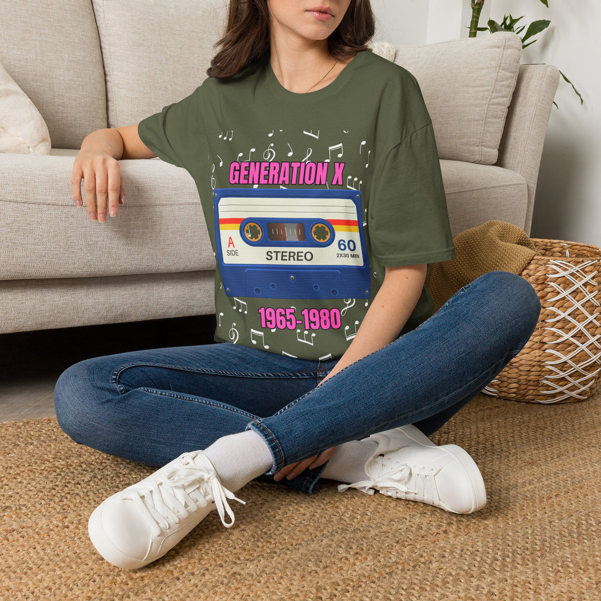 A woman sitting on a woven rug in front of a beige sofa, wearing a green graphic t-shirt with a retro cassette tape design that reads 'GENERATION X 1965-1980' surrounded by music notes