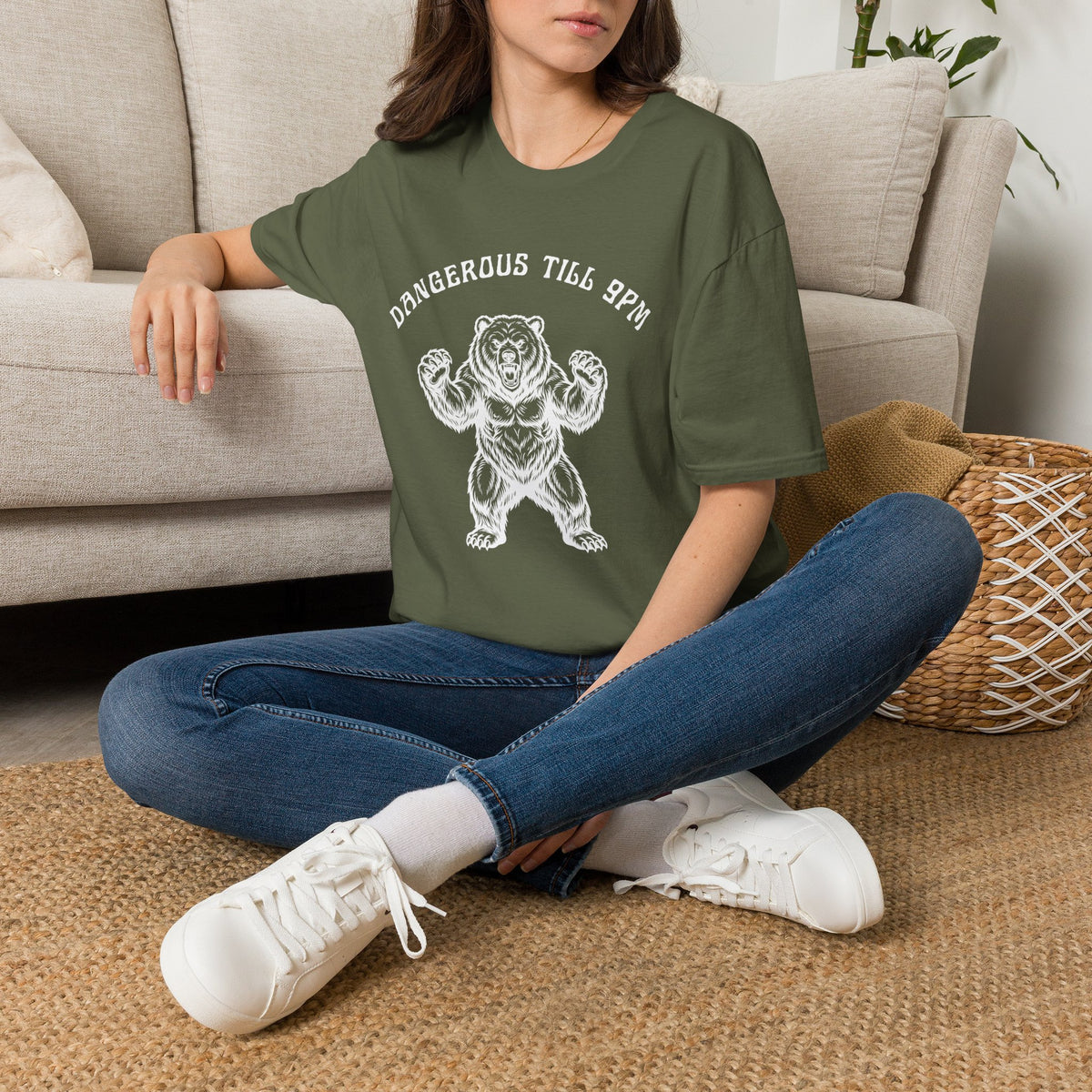 Person wearing a green t-shirt with a white bear with text "Dangerous till 9pm" sitting on the floor in a living room.