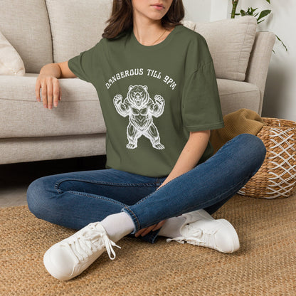 Person wearing a green t-shirt with a white bear with text "Dangerous till 9pm" sitting on the floor in a living room.