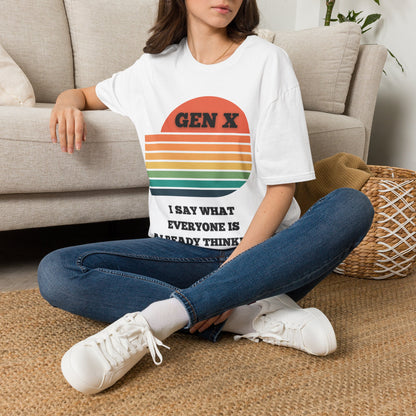 A woman sitting on a woven rug in front of a beige sofa, wearing a white graphic T-shirt with a retro sunset design and the text 'GEN X I SAY WHAT EVERYONE IS ALREADY THINKING'.